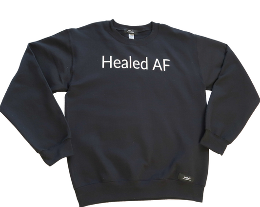 Long sleeve cozy black colored crewneck sweater with white vinyl lettering with phrase “Healed AF”